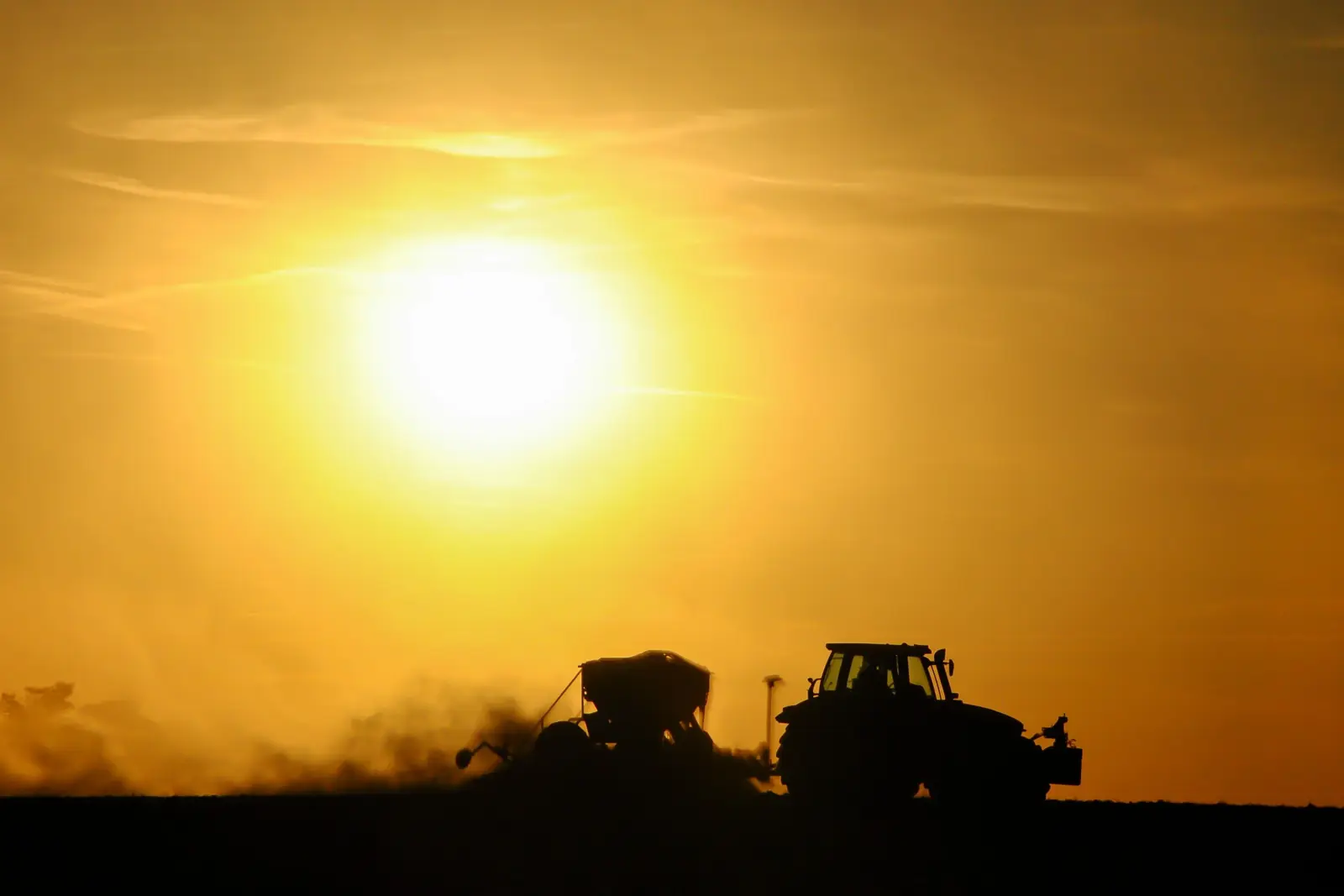 A tractor planting a field at sunrise
