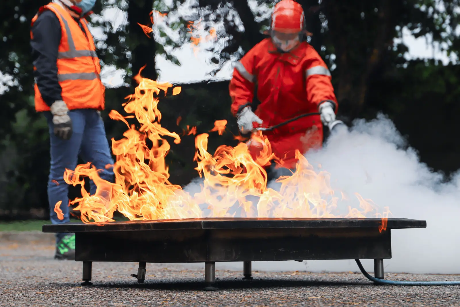 A trainee puts out a pan fire with an extinguisher while an instructor watches